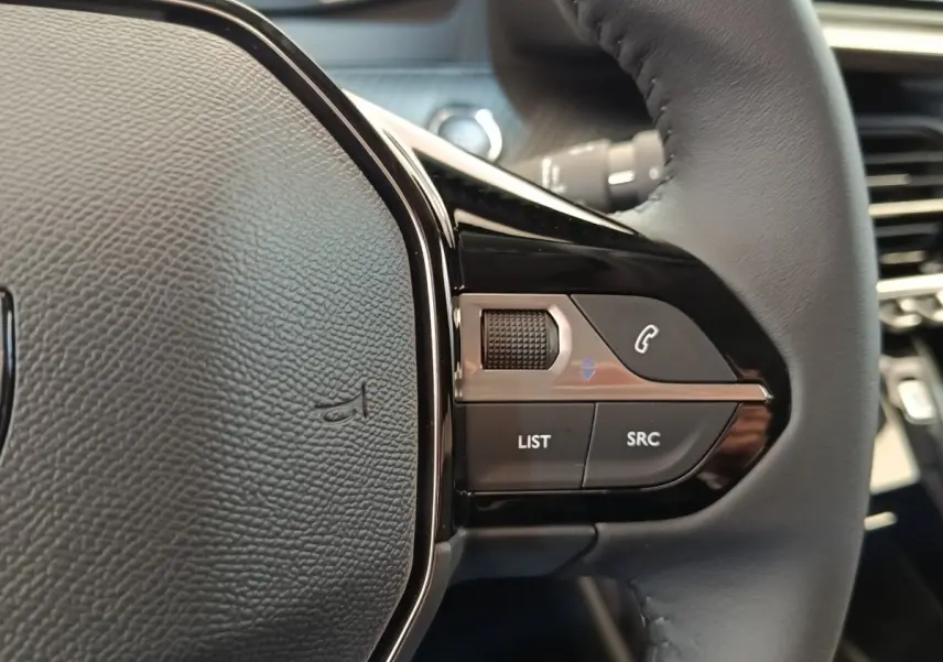 Gros plan sur les commandes multifonctions à droite du volant cuir noir du Peugeot 208 électrique blanc 2024.