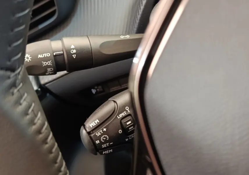 Gros plan sur la commande multifonction du régulateur de vitesse au volant cuir noir du Peugeot 208 électrique blanc.