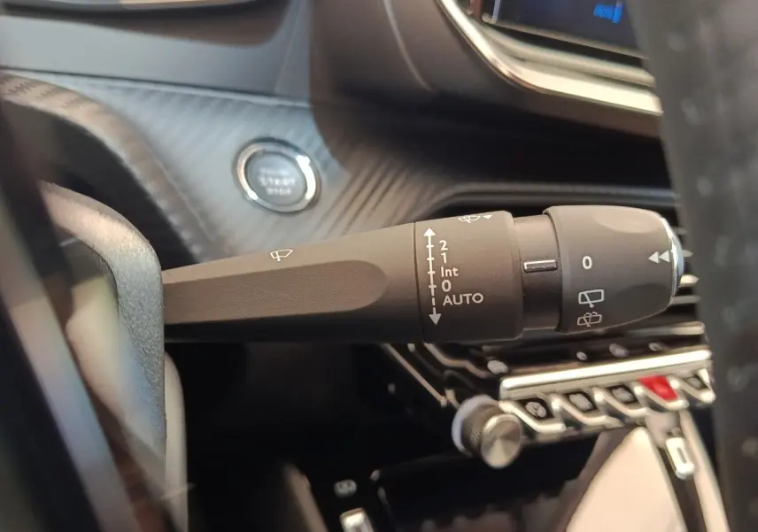 Gros plan sur la commande d’essuie-glace et le bouton démarrage dans l’habitacle noir d’une Peugeot 208 électrique blanche.