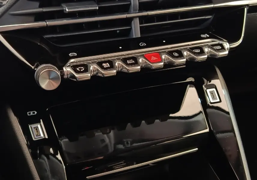 Gros plan sur la console centrale noire brillante du Peugeot 208 électrique 2024 avec commandes tactiles et boutons métalliques.