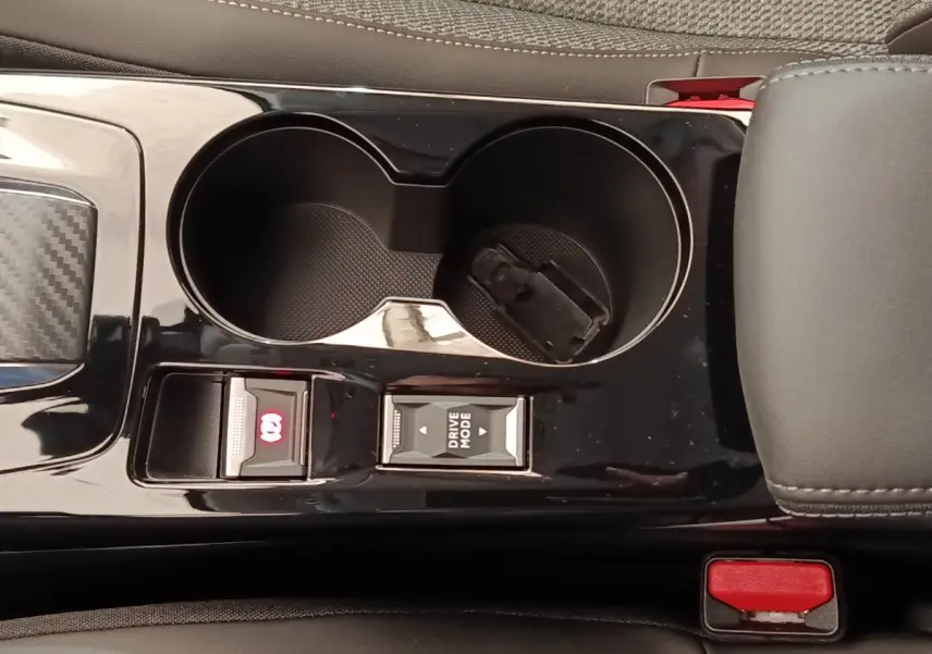 Gros plan sur la console centrale noire de la Peugeot 208 électrique 2024, avec porte-gobelets et commandes frein à main et mode de conduite.