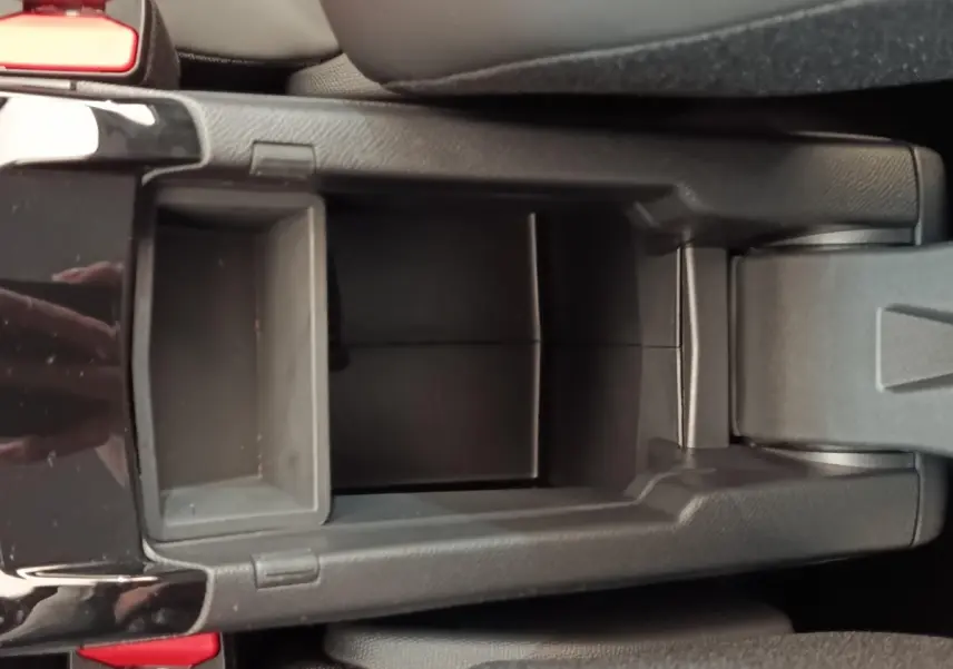 Vue plongeante sur le rangement central noir de la Peugeot 208 électrique 2024, avec accoudoir et bouton de frein à main.