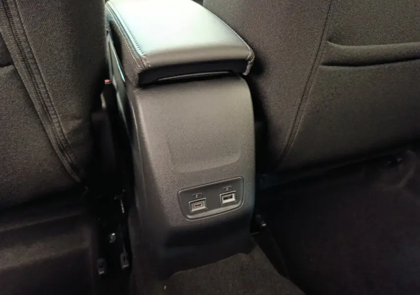 Vue rapprochée de la console centrale arrière noire avec ports USB dans l’habitacle du Peugeot 208 électrique blanc.