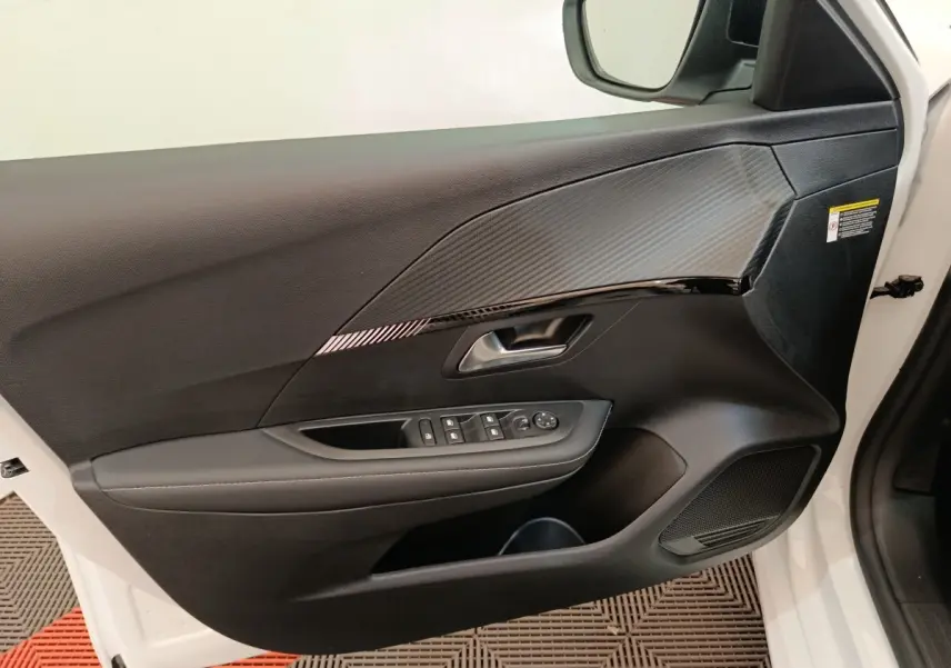 Intérieur côté conducteur de la porte avant droite blanche du Peugeot 208 électrique 2024 avec commandes de vitres et miroir.