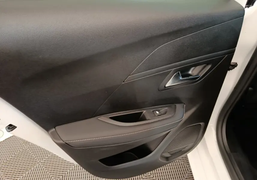 Gros plan sur la porte avant droite noire avec poignée argentée et commande de lève-vitre d’une Peugeot 208 blanche électrique 2024.