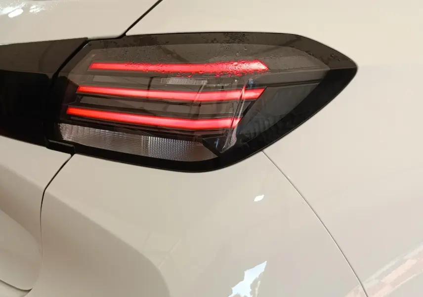 Gros plan sur le feu arrière droit allumé d’une Peugeot 208 électrique blanche, soulignant son design moderne.