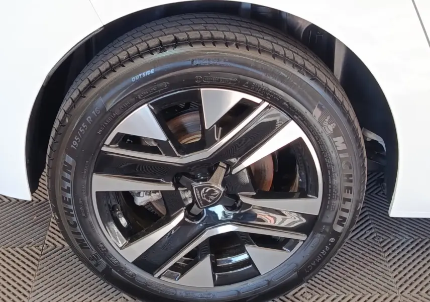 Gros plan sur la roue avant droite d’une Peugeot 208 électrique blanche, jante alliage noir et argent.