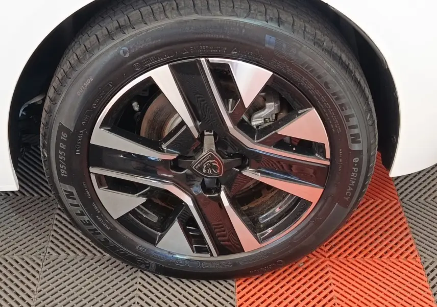 Gros plan sur la roue avant droite de la Peugeot 208 électrique blanche, jante alliage bicolore moderne.