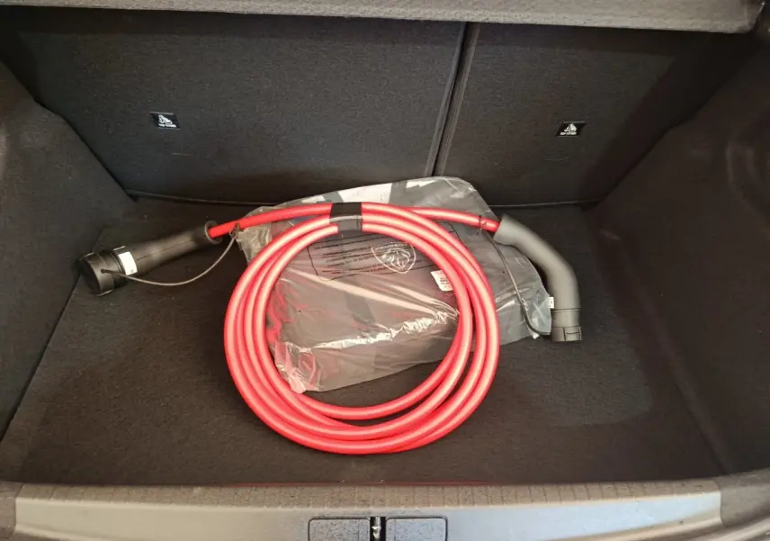Coffre ouvert d'une Peugeot 208 électrique 2024, montrant un câble de charge rouge enroulé sur fond noir.
