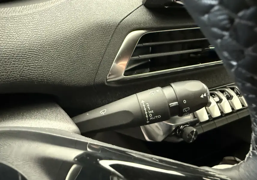 Gros plan sur la manette d’essuie-glace à gauche du volant dans l’habitacle noir du Peugeot 3008 gris 2023.