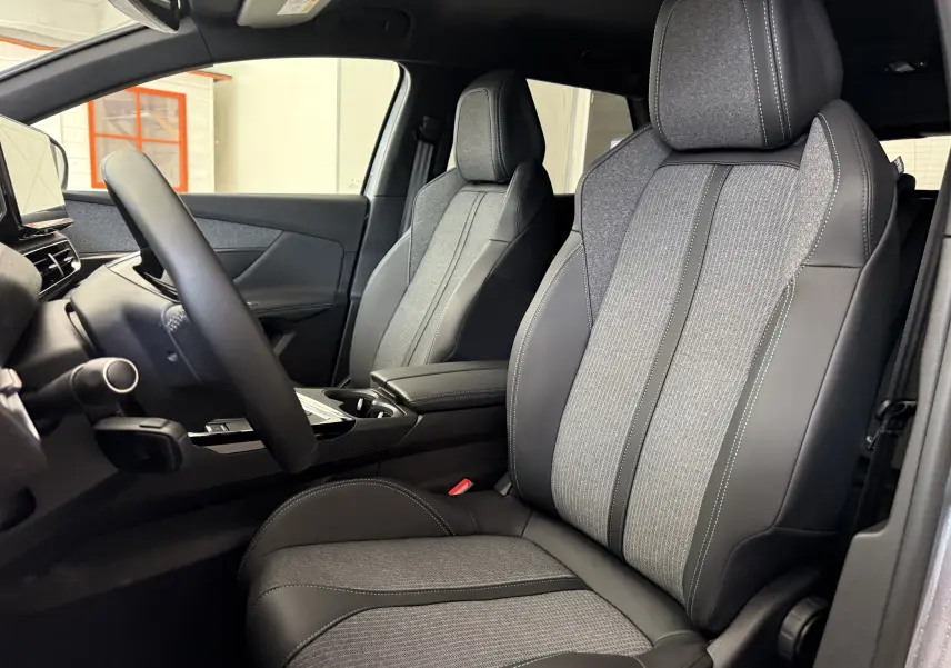 Vue intérieure côté conducteur du Peugeot 3008 2023, sièges tissu gris et cuir noir avec surpiqûres bleues.