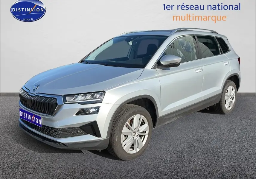 Skoda Karoq gris 3/4 avant droit, avec calandre noire et jantes alliage visibles sur sol gris.