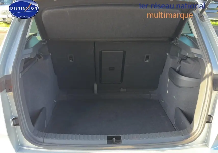 Coffre ouvert vu de l'arrière d'un Skoda Karoq gris, montrant l'espace de chargement et la trappe à skis centrale.