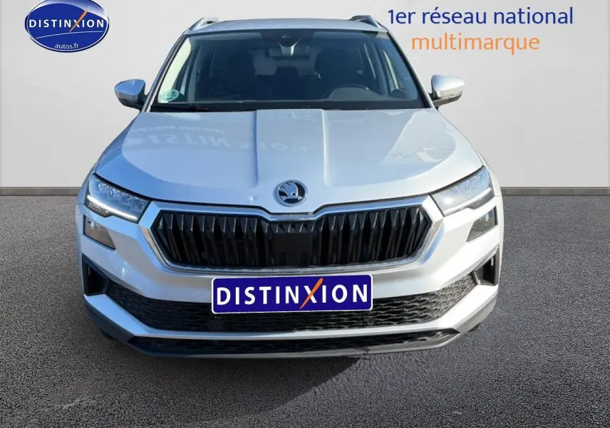 Vue avant d'un Skoda Karoq gris 2025 avec calandre noire et phares LED, sur fond neutre avec logo Distinxion.