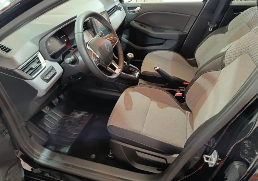 Vue intérieure côté conducteur de la Renault Clio noire 2025, montrant sièges tissu gris et tableau de bord avec volant multifonctions.