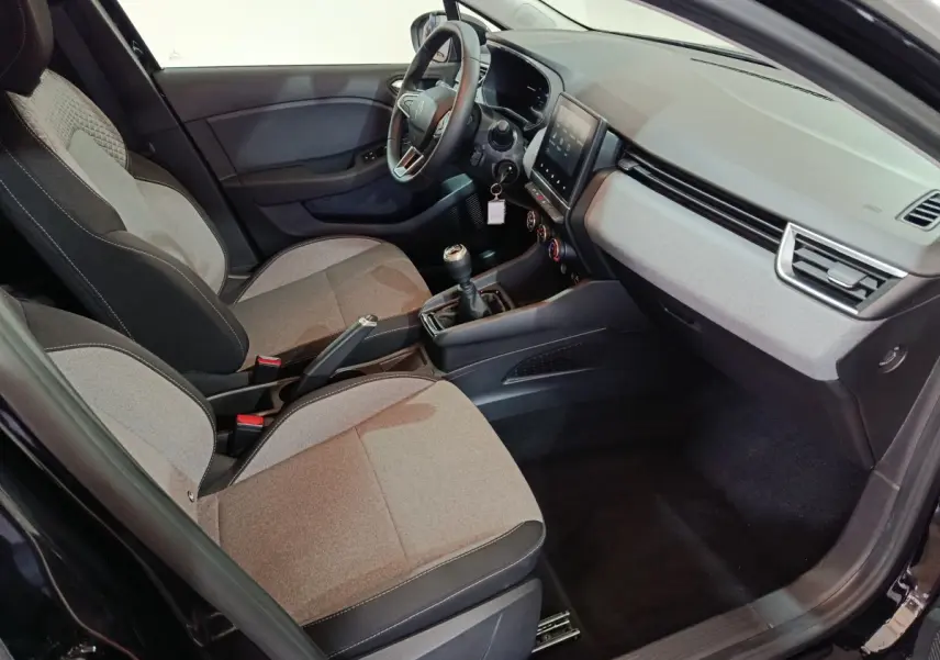 Vue intérieure côté conducteur de la Renault Clio noire 2025, montrant sièges tissu, volant multifonctions et écran tactile central.