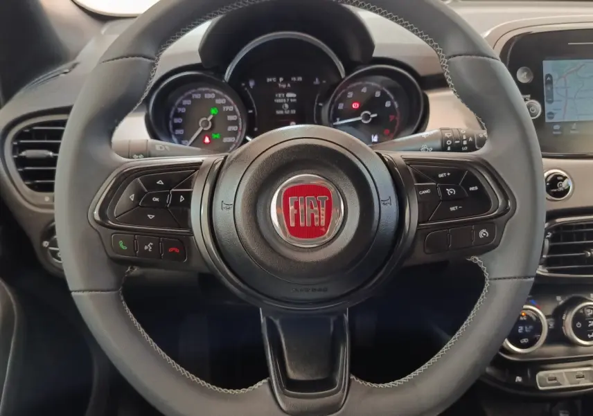 Vue rapprochée du volant cuir gris avec logo FIAT rouge et tableau de bord numérique de la 500X 2021.
