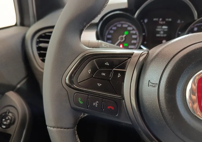 Gros plan sur les commandes gauche du volant cuir de la FIAT 500X gris foncé, avec tableau de bord en arrière-plan flou.