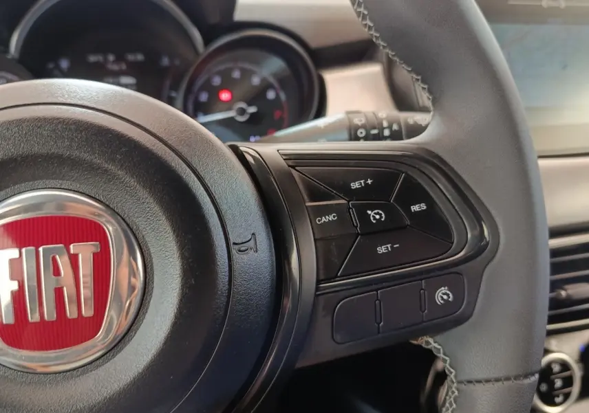Vue rapprochée du volant cuir noir de la FIAT 500X 2021 avec commandes de régulateur de vitesse et logo rouge FIAT.