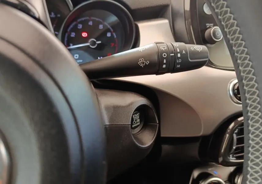 Gros plan intérieur sur le bouton démarrage et la commande d’essuie-glace à gauche du volant d’une Fiat 500X gris foncé.