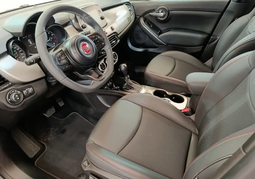 Intérieur avant droit de la Fiat 500X gris foncé, volant multifonctions, sièges cuir noir avec surpiqûres rouges.