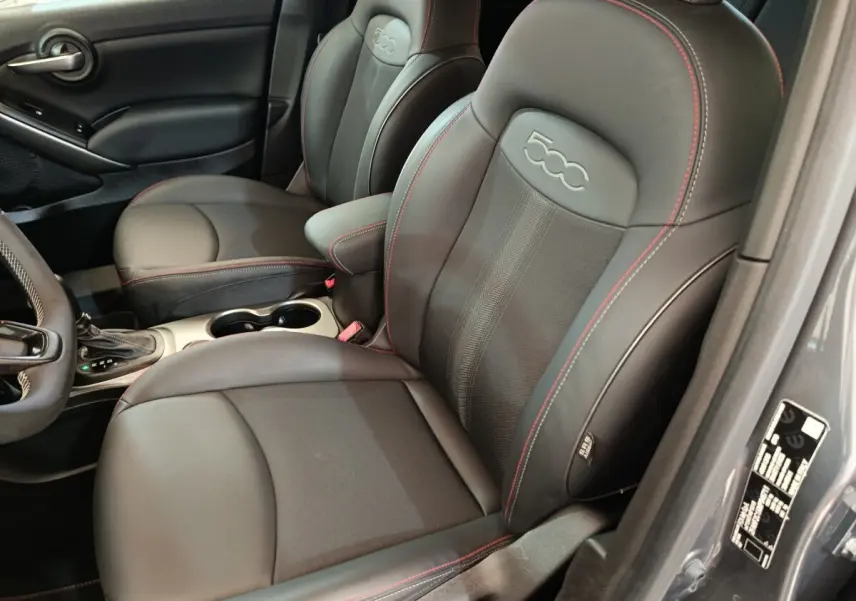 Vue intérieure côté conducteur du Fiat 500X 2021 gris foncé, sièges en cuir noir avec surpiqûres rouges et logo 500 embossé.