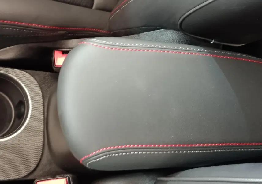 Détail de l'accoudoir central noir avec surpiqûres rouges dans l'habitacle de la Fiat 500X gris foncé.