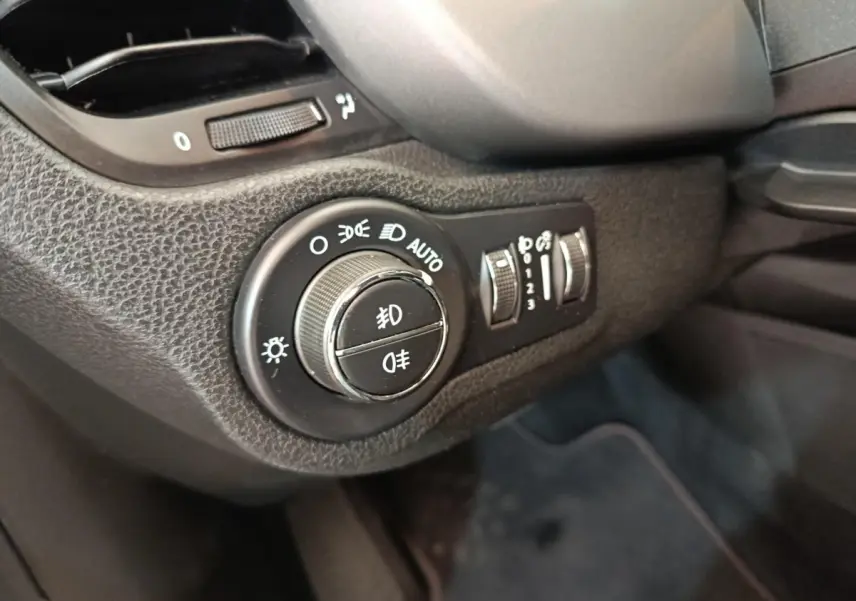 Gros plan sur la molette de réglage des phares et commandes d’éclairage intérieures d’une Fiat 500X gris foncé, côté conducteur.