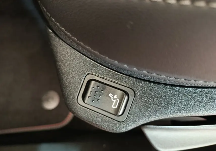 Bouton de réglage électrique de siège en gros plan sur l'assise en cuir marron foncé d'une Fiat 500X gris foncé.