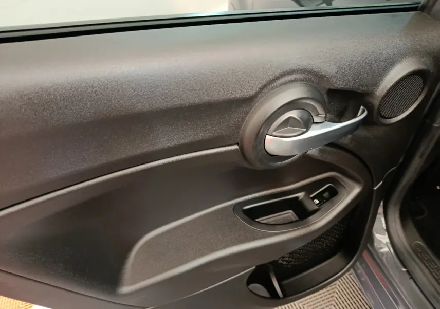 Vue intérieure côté gauche de la porte avant d’une FIAT 500X gris foncé avec poignée argentée et commande de vitre électrique.