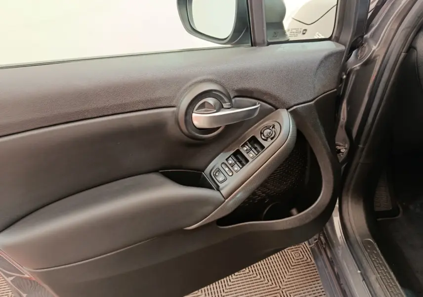 Intérieur côté conducteur de la FIAT 500X gris foncé, montrant la porte avec commandes des vitres et rétroviseur.