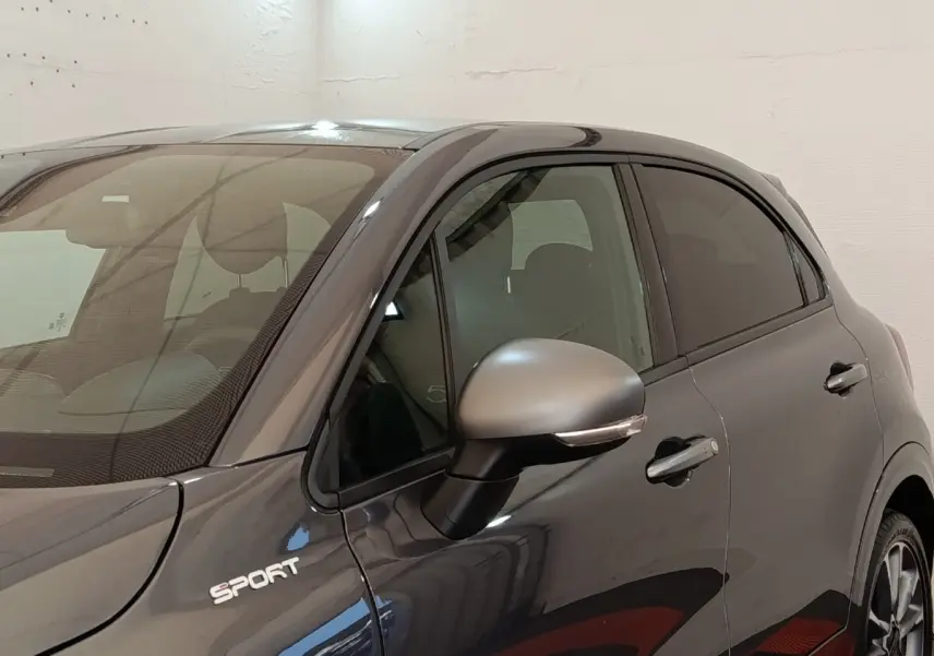 Vue de côté droit avant d'une FIAT 500X gris foncé avec badge Sport et rétroviseur assorti.