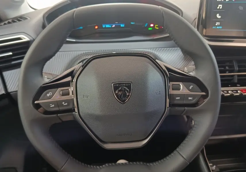 Vue rapprochée du volant cuir multifonctions noir de la Peugeot 208 électrique 2024 avec tableau de bord numérique en arrière-plan.