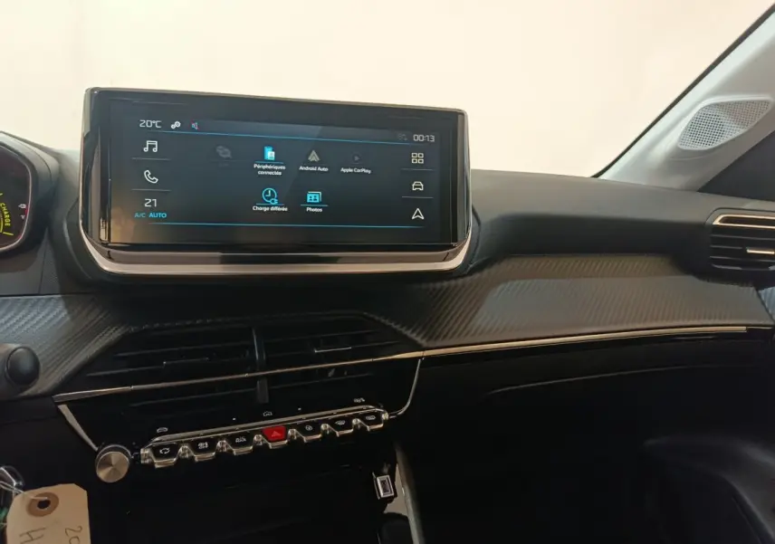 Vue intérieure du tableau de bord de la Peugeot 208 électrique 2024 avec écran tactile central et finition carbone gris.