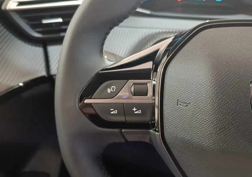 Gros plan sur le côté gauche du volant cuir noir du Peugeot 208 électrique 2024 avec commandes multifonctions.