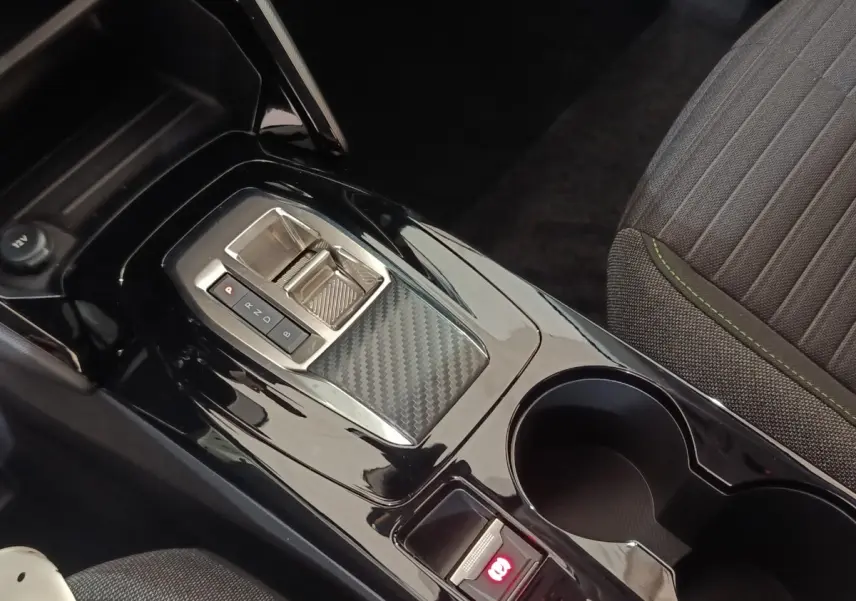 Gros plan sur la console centrale noire brillante de la Peugeot 208 électrique 2024 avec frein à main électrique et porte-gobelets.