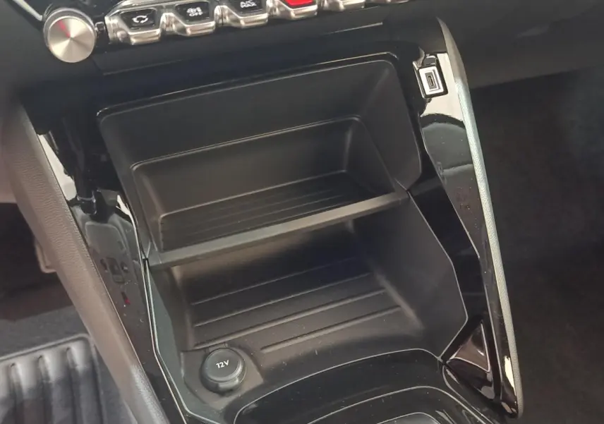 Vue rapprochée de la console centrale noire avec prise 12V et rangement sur la Peugeot 208 électrique gris clair.