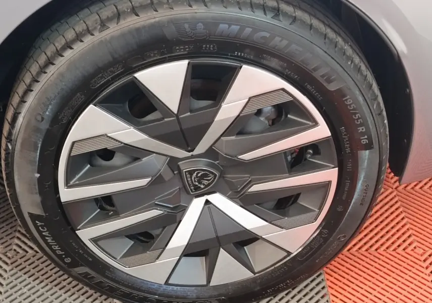 Gros plan sur la roue avant droite de la Peugeot 208 électrique gris clair avec jante au design géométrique noir et argent.