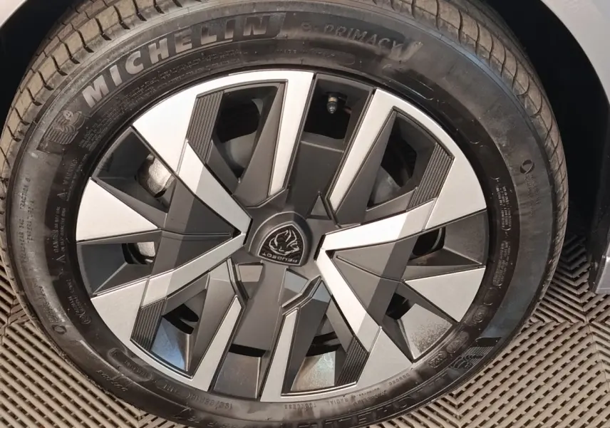 Gros plan sur la roue avant droite d’une Peugeot 208 électrique gris clair, jante au design géométrique moderne.