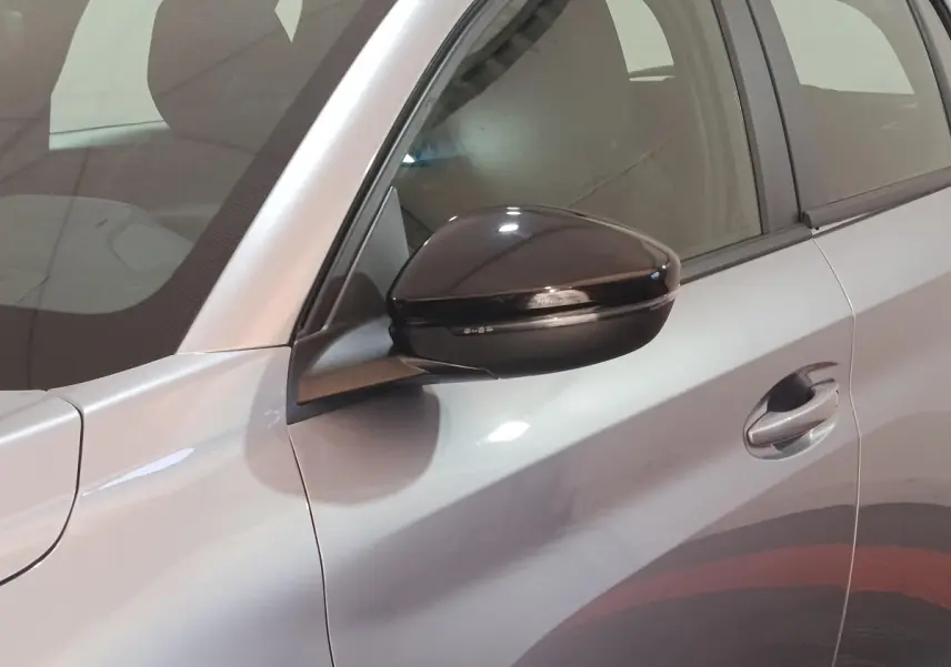 Gros plan sur le rétroviseur noir et la portière côté gauche d'une Peugeot 208 électrique gris clair.