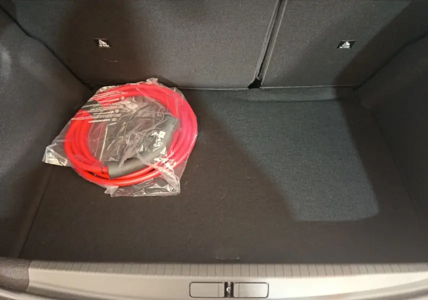 Coffre de Peugeot 208 électrique gris clair vu de dessus, avec câble de recharge rouge emballé posé à gauche.