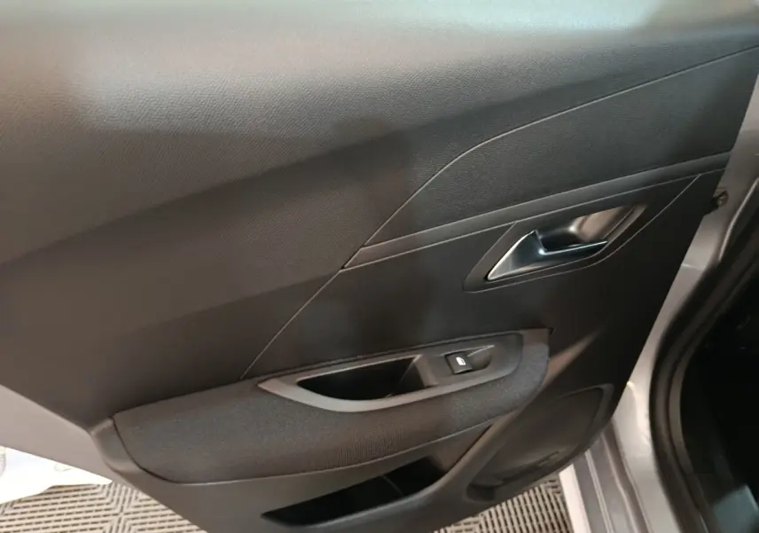 Vue intérieure côté droit de la porte avant d'une Peugeot 208 électrique gris clair avec bouton de lève-vitre et poignée métallique.