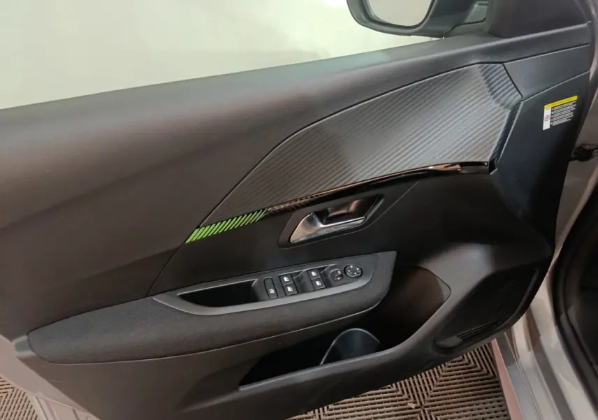 Vue intérieure côté gauche de la porte avant d’une Peugeot 208 électrique gris clair avec insert décoratif et commandes vitres.
