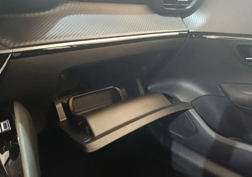 Intérieur de la Peugeot 208 électrique 2024, vue côté passager sur la boîte à gants ouverte avec finition noire et carbone.