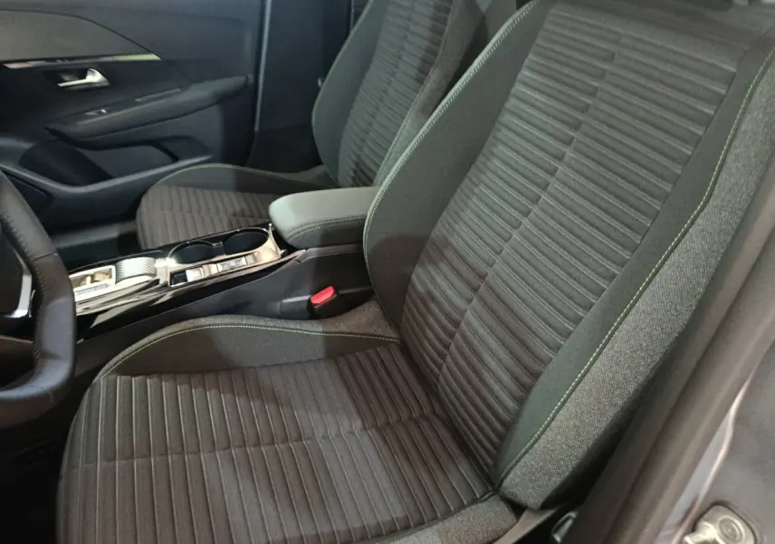 Vue intérieure côté conducteur de la Peugeot 208 électrique 2024, sièges tissu gris foncé avec surpiqûres vertes et console centrale.
