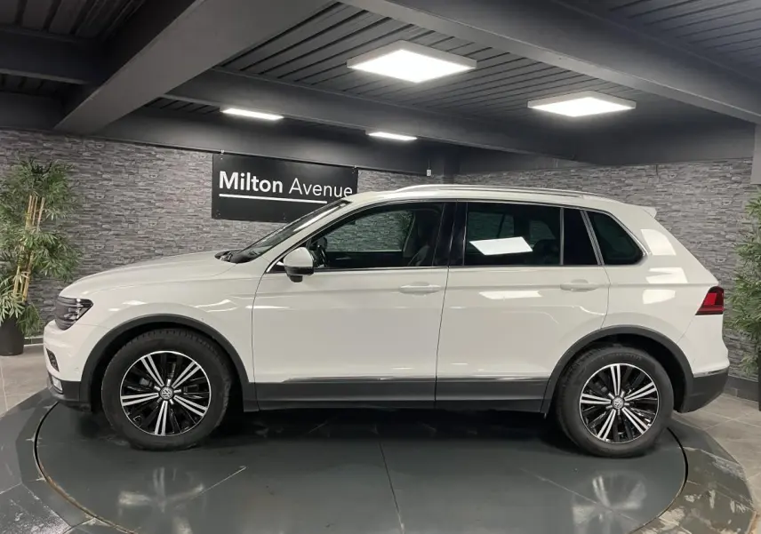 Vue de profil côté gauche d'un Volkswagen Tiguan blanc avec jantes alliage noires et décorations noires basses.