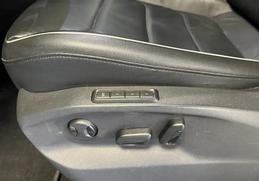 Gros plan sur les commandes de réglage électrique du siège conducteur en cuir noir du Volkswagen Tiguan blanc.