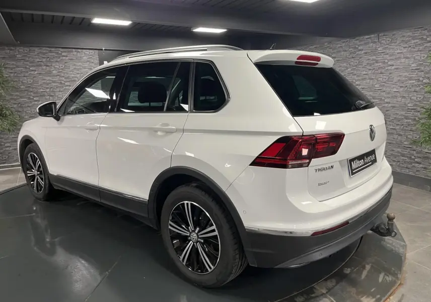 Volkswagen Tiguan blanc vu en 3/4 arrière droit, avec jantes alliage noires et crochet d'attelage escamotable.