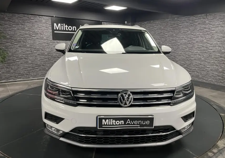 Volkswagen Tiguan blanc vu de face, avec calandre chromée et phares LED dans un showroom intérieur.