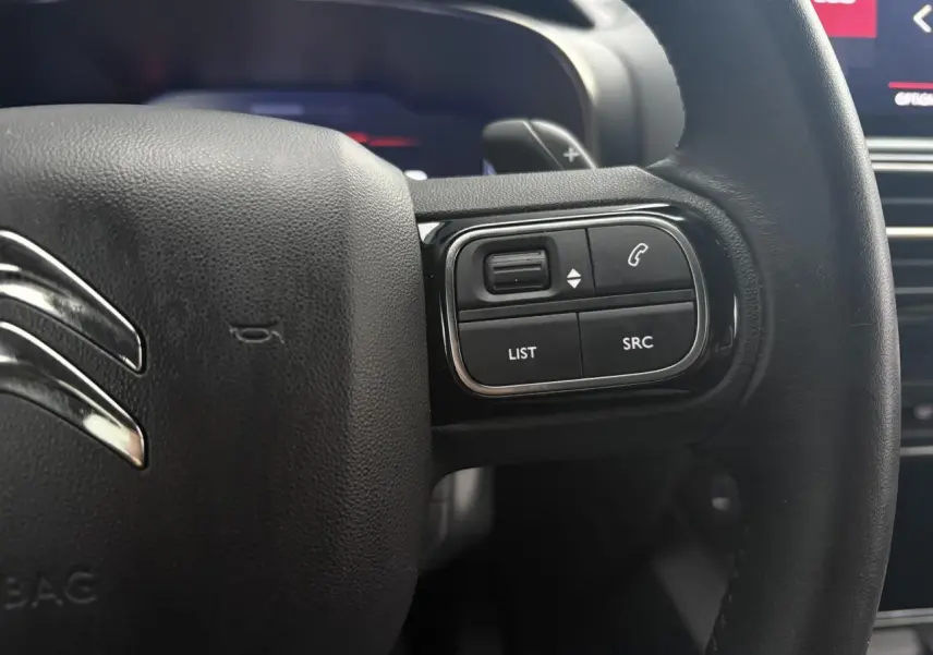 Gros plan sur le volant noir en cuir du Citroën C5 Aircross Hybrid 2024 avec commandes intégrées côté droit.
